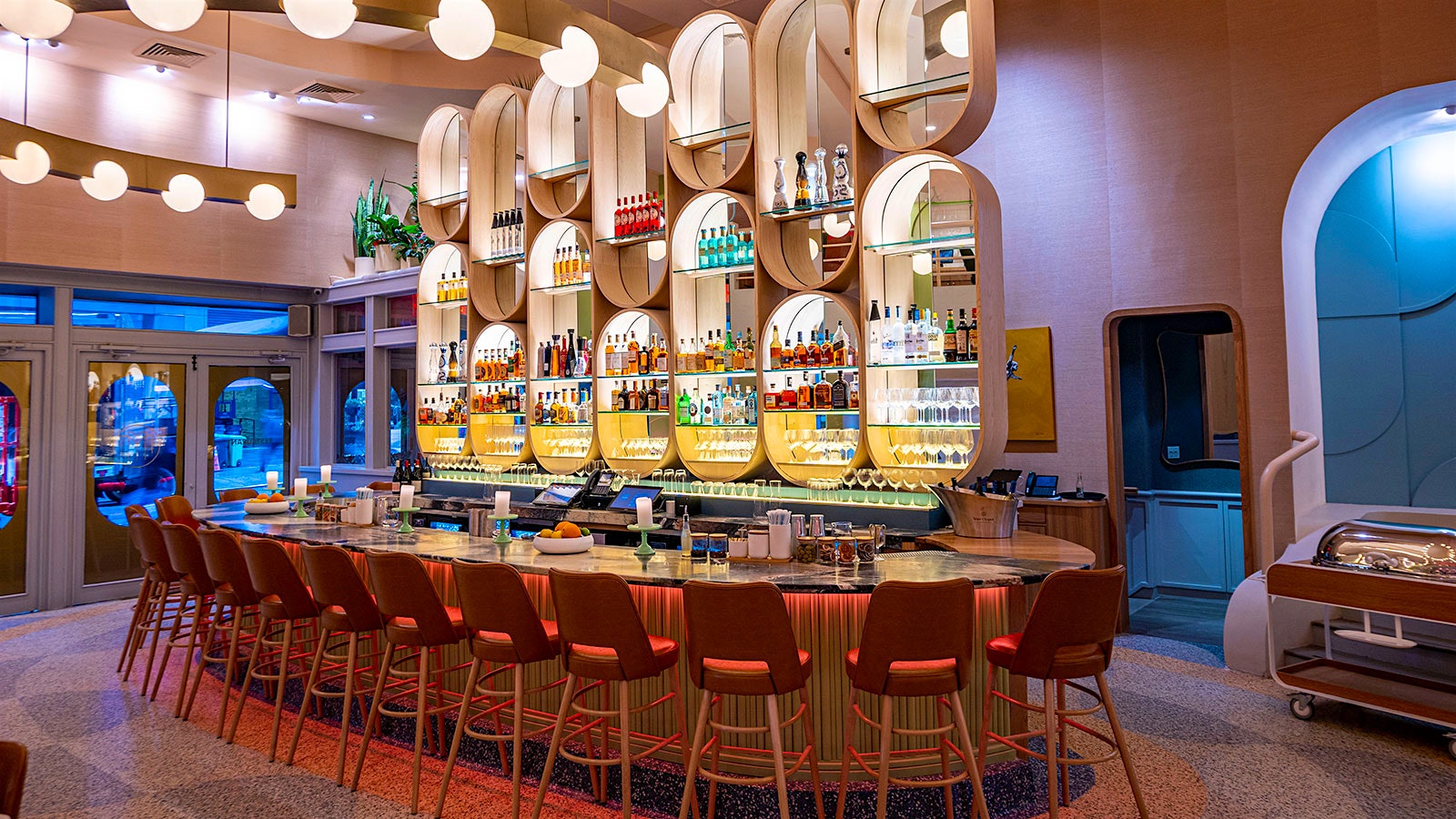  El Bar Monterey curvo está brillantemente iluminado con bombillas esféricas, con estantes retroiluminados en forma de huevo llenos de botellas de licor y vino y cristalería.